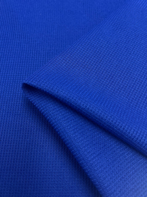 Close-up image of blue Waffle Knit - Cobalt - 170cm fabric by Super Cheap Fabrics with a fine, grid-like texture. The fabric is layered, showing two sections overlapping each other, highlighting the weave and color, creating a subtle three-dimensional effect.