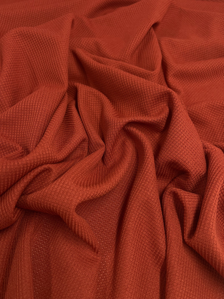 A close-up view of a crumpled piece of Super Cheap Fabrics' Waffle Knit - Rooibos Tea - 170cm with a textured surface and soft folds. The material appears to be smooth and lightweight, creating gentle shadows and highlights that give it a subtle three-dimensional appearance.
