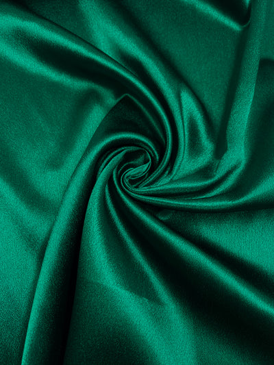 Close-up of a piece of Super Cheap Fabrics Satin Back Crepe - Antique Green - 150cm fabric, featuring a swirling fold in the center. The silky texture and rich color are highlighted by the way the light reflects off its surface, making it perfect for elegant evening wear.