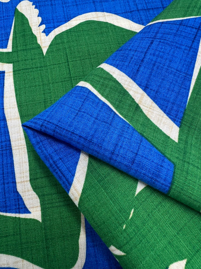 A close-up view of a lightweight fabric with a blue and green abstract design, possibly depicting animal silhouettes. Made from soft Bamboo Rayon - Dance Indigo - 150cm by Super Cheap Fabrics, the material appears to be folded neatly at one corner, showcasing the pattern and texture of the beginner-friendly nature fabric.