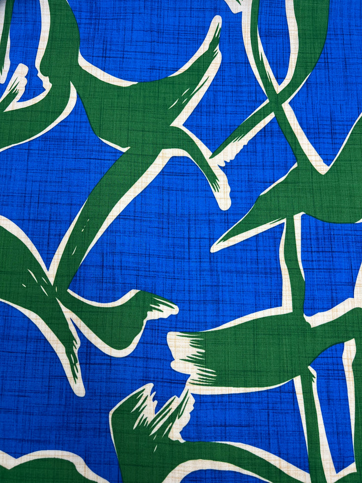 A vibrant pattern on a blue background featuring abstract green and white bird-like shapes in dynamic poses. This stylized design, with bold lines and a sense of movement, gives the Bamboo Rayon - Dance Indigo - 150cm by Super Cheap Fabrics an artistic and lively appearance perfect for home decor.