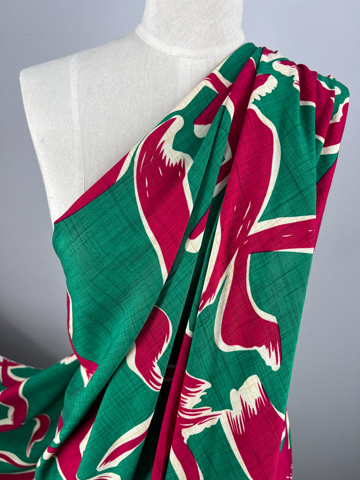 A close-up of a mannequin draped in vibrant Bamboo Rayon - Dance Pepper Green - 150cm fabric from Super Cheap Fabrics with an abstract floral pattern. The lightweight fabric showcases large, bold flowers in maroon with white outlines and green backgrounds, creating a striking contrast against the light-colored mannequin.