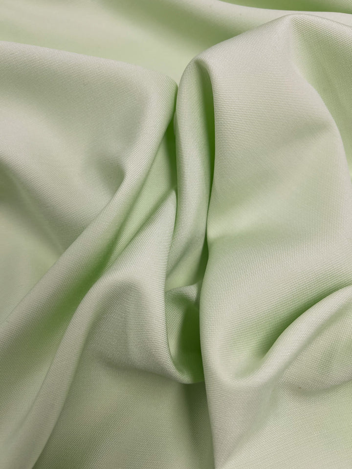 A close-up shot of *Suiting - Ambrosia - 140cm* by *Super Cheap Fabrics*, draped and folded, showing gentle creases and a smooth texture. The diagonal weave pattern adds to the material's lightweight and silky appearance.