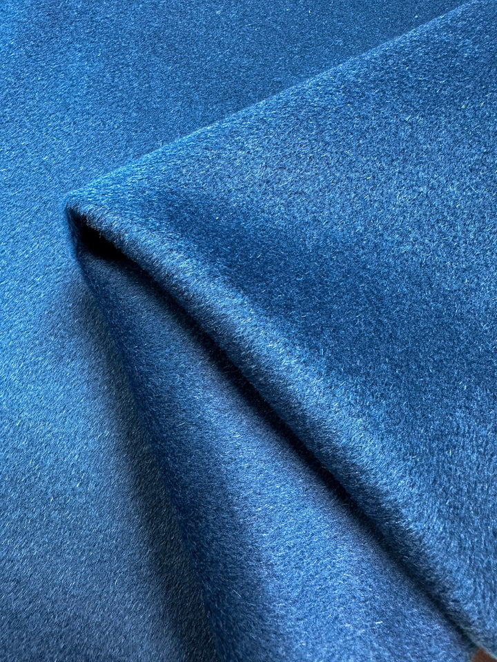 A close-up of a folded piece of Wool Cashmere - Mykonos Blue - 150cm from Super Cheap Fabrics. The material appears smooth and has a subtle sheen, suggesting it could be velvet or similarly plush wool fabric. The folds create shadows, emphasizing the fabric's luxurious quality.