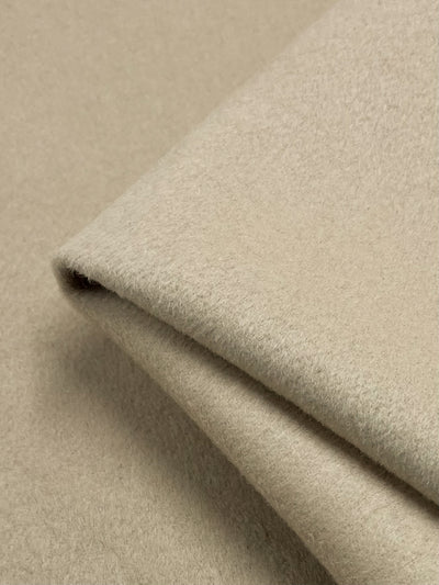 A close-up image of a folded beige fabric, resembling the texture of a thick Wool Cashmere - Frappe - 150cm from Super Cheap Fabrics. The material appears soft and slightly fuzzy, perfect for outer coats.