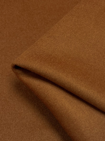 Close-up of a folded piece of **Super Cheap Fabrics Wool Cashmere - Leather Brown - 150cm**. The texture appears soft and smooth, similar to thick wool cashmere fabric, and the edges are neatly folded to form a sharp corner. The lighting highlights the fabric's texture and color variations subtly.