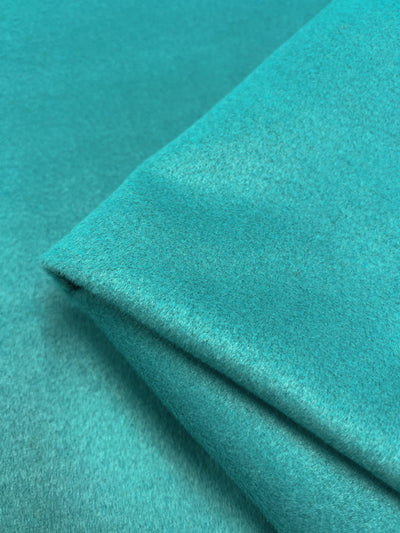 A close-up photo of a piece of Super Cheap Fabrics' Wool Cashmere - Peacock - 150cm fabric, folded over itself, displaying its smooth texture and vibrant color.