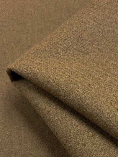 A close-up image of a folded piece of medium weight, brown woolen fabric, Designer Wool - Coca Mocha - 150cm by Super Cheap Fabrics. The texture appears soft and fine, showcasing the weave and material quality. The fabric is arranged with gentle folds, creating a sense of depth and dimension.