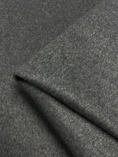 Close-up of two overlapping layers of Wool Cashmere - Charcoal - 150cm by Super Cheap Fabrics, showcasing its soft, smooth texture and fine fibers. The medium weight fabric is aligned diagonally, with one layer partially covering the other, highlighting the material's thickness and quality.
