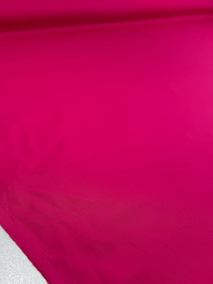 The Plain Cotton - Fuchsia - 150cm from Super Cheap Fabrics features a vibrant color and soft texture, with gentle folds and shadows visible in its lightweight cotton material.