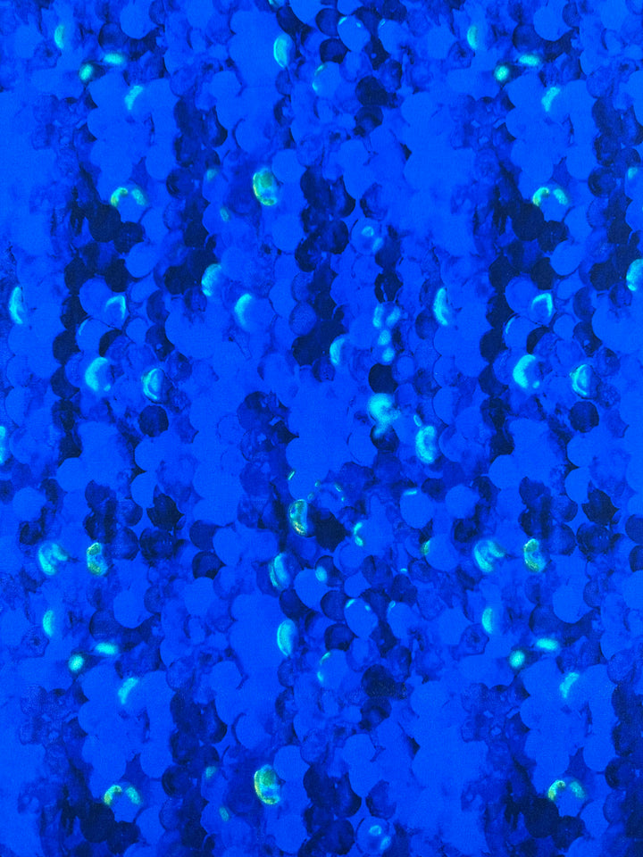 A pattern of small, circular shapes in various shades of blue adorns this medium-weight fabric. The circles are densely packed, creating a textured, almost holographic appearance with some areas glowing in greenish tones. Made from polyester/spandex fabric, the overall effect is vibrant and dynamic. Introducing Printed Lycra - Scales - 150cm from Super Cheap Fabrics.
