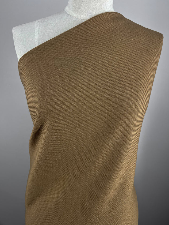 A mannequin draped with a single piece of Twill Suiting - Aztec - 138cm by Super Cheap Fabrics that covers one shoulder, leaving the other exposed. The background is a solid grey, highlighting the rich texture and color of the twill suiting.