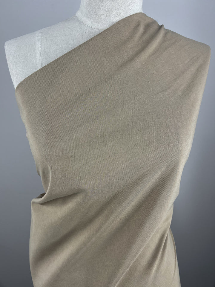 A mannequin draped with Linen Blend - Tannin - 150cm by Super Cheap Fabrics, showcasing the texture and flow of the material. The designer fabric is wrapped asymmetrically over the shoulder, highlighting its smooth and soft appearance against the neutral gray background.