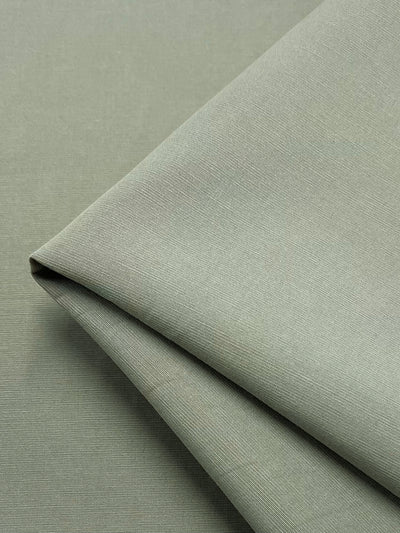 A close-up image of a piece of light green Super Cheap Fabrics’ Linen Blend - Elm - 150cm with a smooth, slightly textured surface. The fabric is neatly folded at one corner, showcasing its even weave and clean finish.