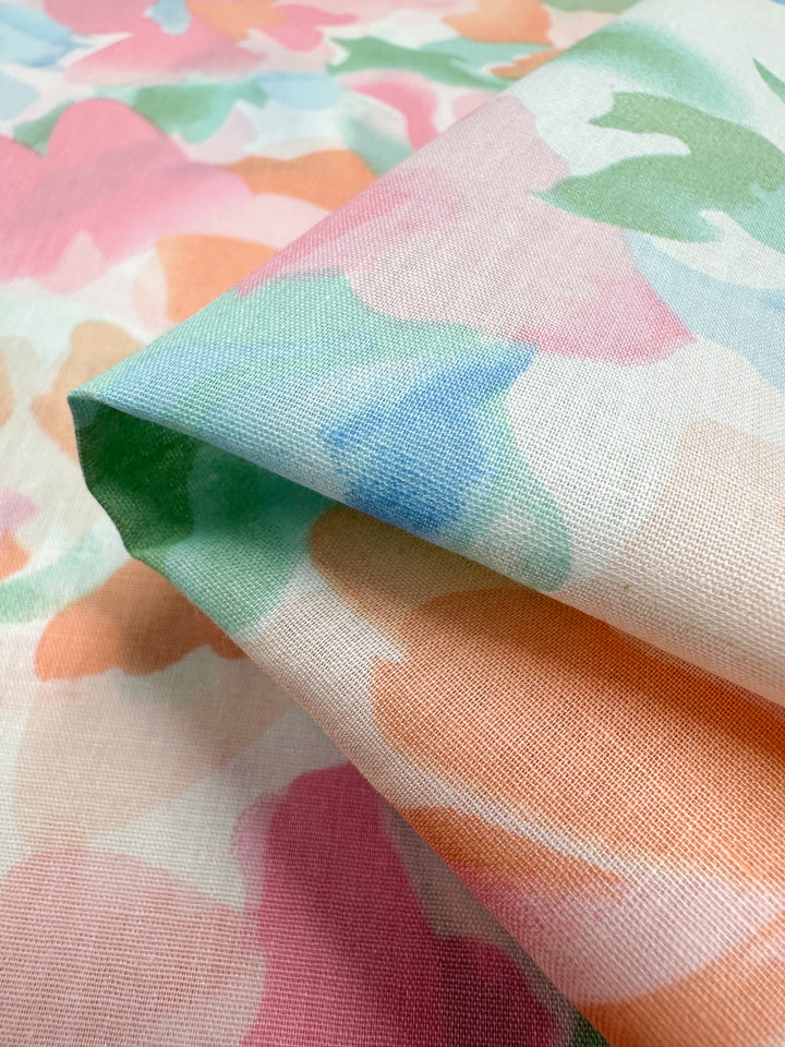 Close-up of the "Printed Cotton - Blossoms - 150cm" by Super Cheap Fabrics, featuring an abstract floral pattern in pastel shades of pink, green, blue, and orange. The natural cotton fibers are folded to highlight its smooth texture and vibrant design ideal for various uses.