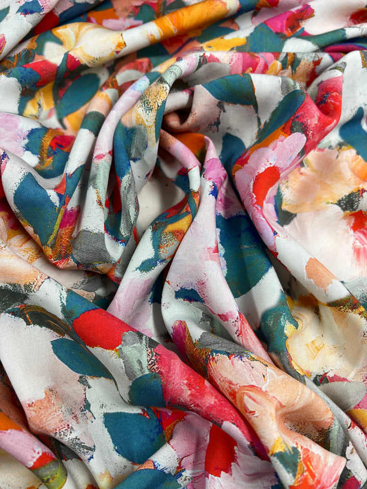 A close-up of a piece of Designer Rayon - Botanical - 145cm from Super Cheap Fabrics adorned with a vibrant abstract floral pattern. The design features bold splashes of red, blue, green, pink, and yellow hues, giving the fabric a lively, artistic appearance. Softly draped with gentle folds and shadows, it is a versatile choice for any project.