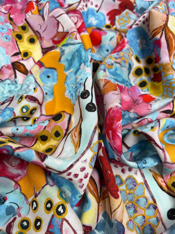 A vibrant piece of Designer Rayon - Impressionist - 145cm from Super Cheap Fabrics featuring an abstract pattern with colorful flowers, leaves, and various shapes in shades of pink, blue, yellow, and red. The fabric is crumpled, creating textured folds and shadows— a true showcase of vibrant prints in versatile fabric form.
