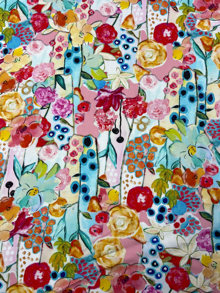 A vibrant, abstract floral pattern featuring large, colorful flowers in shades of yellow, red, pink, and blue. Bold green leaves and black dotted accents are interspersed among the blooms, all set against a light pink background on versatile Designer Rayon - Festive - 145cm fabric by Super Cheap Fabrics.