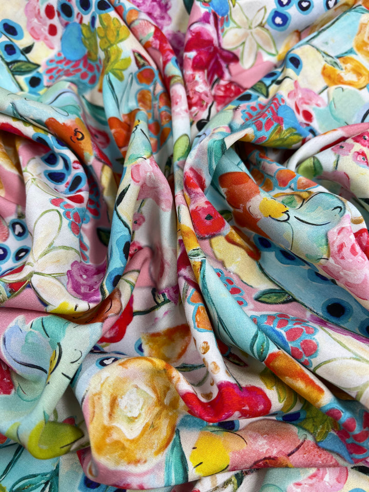 A close-up image of colorful, crumpled fabric with a vibrant floral pattern. This versatile fabric, Designer Rayon - Festive - 145cm by Super Cheap Fabrics, features a mix of flowers in hues of pink, red, yellow, blue, and green, creating an intricate and lively design—perfect for those who appreciate vibrant prints.