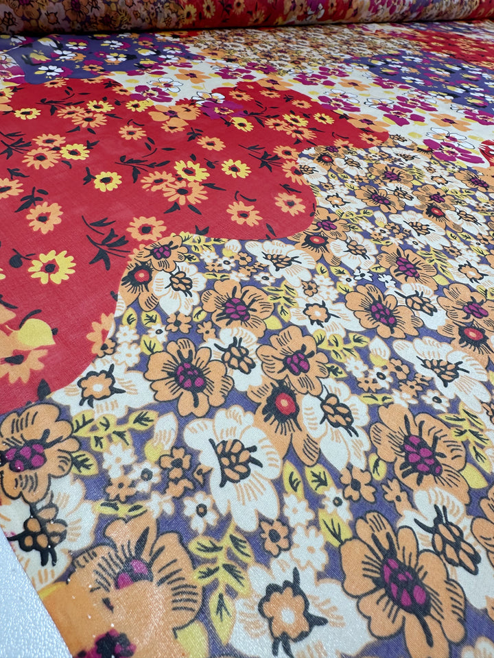 A detailed view of the vibrant Florazard fabric by Super Cheap Fabrics, perfect for dressmaking. This extra lightweight silk material features overlapping red, orange, yellow, and purple flowers on a white background, showcasing a mix of small and large blooms in its intricate pattern. With a width of 140cm, it combines elegance with a burst of color.