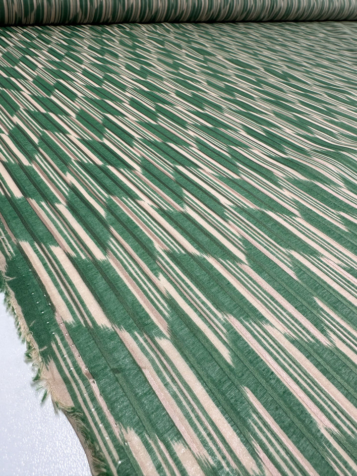 In a textile workshop, the "Printed Silk - Escalate - 140cm" from Super Cheap Fabrics is displayed, featuring a captivating abstract zigzag pattern in green and beige. This extra light weight fabric offers a smooth texture with fringed ends, making it an ideal choice for crafting elegant dresses.