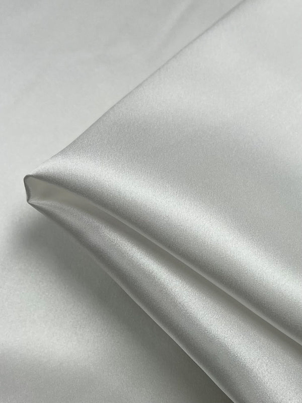 Close-up of a folded piece of white Silk Satin - Off White - 138cm by Super Cheap Fabrics, showcasing its smooth texture and subtle sheen. The luxurious fabric is neatly arranged, with soft folds creating gentle highlights and shadows, emphasizing its suitability for elegant dressy tops.