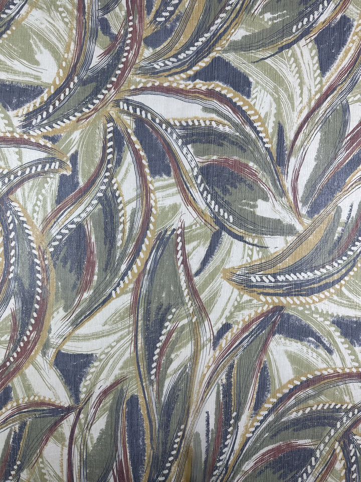 A close-up of the Pure Printed Silk - Feathers from Super Cheap Fabrics, showcasing its dynamic, embroidered pattern. The fabric features a textured abstract design with overlapping leaf motifs in shades of green, brown, beige, and hints of dark blue.