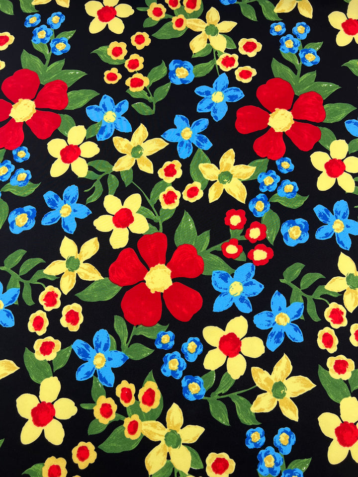 A vibrant floral pattern on a black background, featuring large red flowers, medium yellow flowers, and smaller blue flowers, all with green leaves. The intricate design intersperses the different sized blooms evenly across the Super Cheap Fabrics Deluxe Print - Nursery - Black - 155cm versatile fabric.
