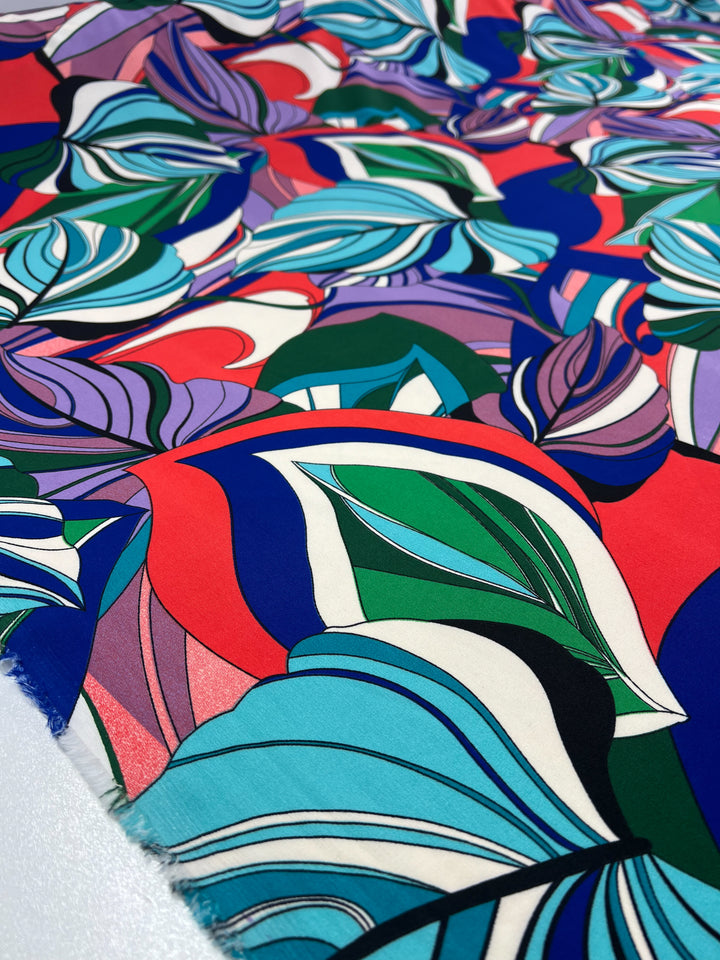 A vibrant, abstract pattern on polyester fabric featuring overlapping organic shapes and curved lines in a bold color palette that includes shades of blue, green, red, and purple. The Deluxe Print - Jungle Tides - 155cm by Super Cheap Fabrics is dynamic and fluid, evoking a sense of movement and energy—ideal for versatile designer fabrics.