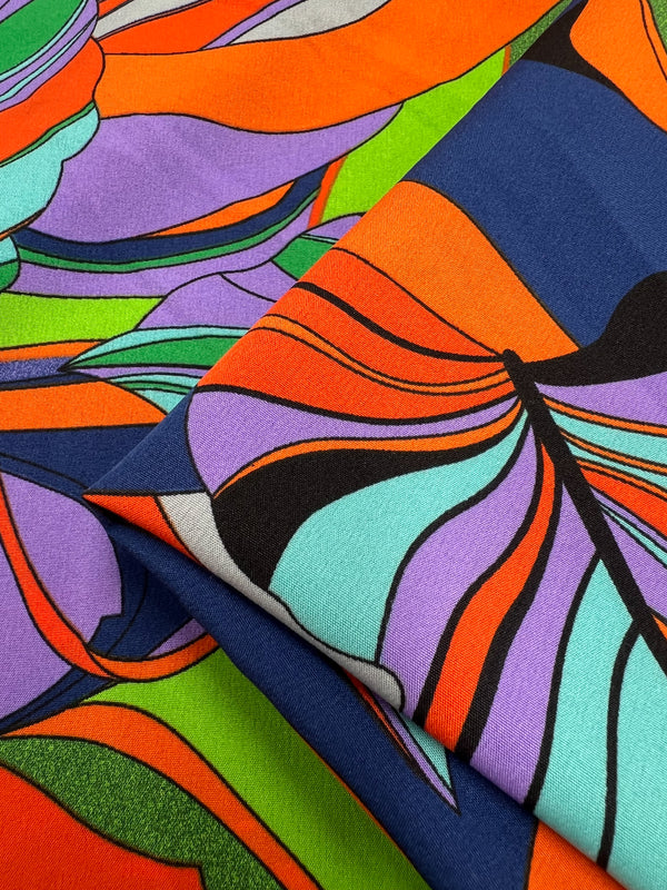 A vibrant polyester fabric featuring bold, colorful abstract patterns. The design includes sweeping shapes in vivid shades of orange, purple, green, blue, black, and turquoise. This bright print has sections that overlap, adding depth and a dynamic flow to the composition—perfect for Deluxe Print - Terra - 155cm by Super Cheap Fabrics.