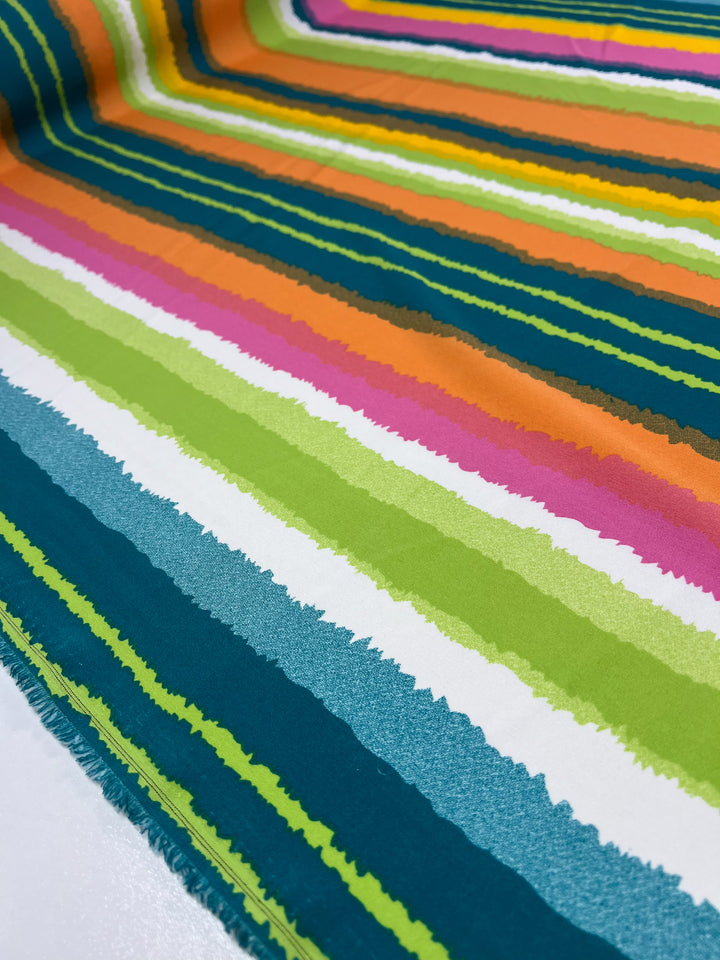 Close-up of a colorful, striped polyester fabric. The pattern features horizontal lines in various vibrant colors, including orange, green, pink, white, and blue, with edges that appear slightly wavy and uneven. This Deluxe Print - Lollipop - 155cm from Super Cheap Fabrics showcases both texture and versatility in its design.
