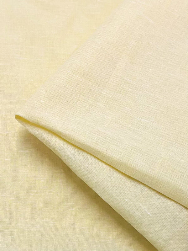 A close-up of light yellow fabric is shown, folded diagonally with a visible crease. The light weight fabric appears to be made of a woven material, possibly linen or cotton. The texture reveals a fine, uniform weave pattern. This is "Linen Voile - French Vanilla - 155cm" by Super Cheap Fabrics.