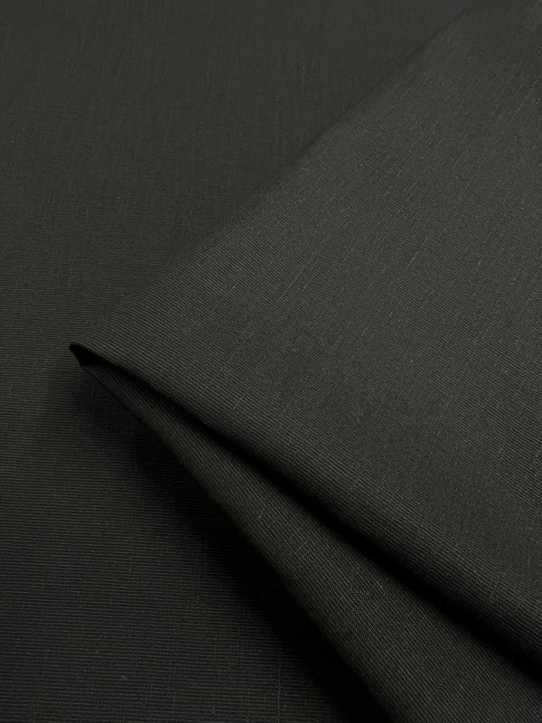 A close-up shot of smooth, black twill *Suiting - Black - 150cm* from *Super Cheap Fabrics* folded over itself. The material appears to have a subtle, fine texture and is neatly arranged, highlighting its seamless and sleek finish. This versatile fabric exudes elegance with its lightweight drape.