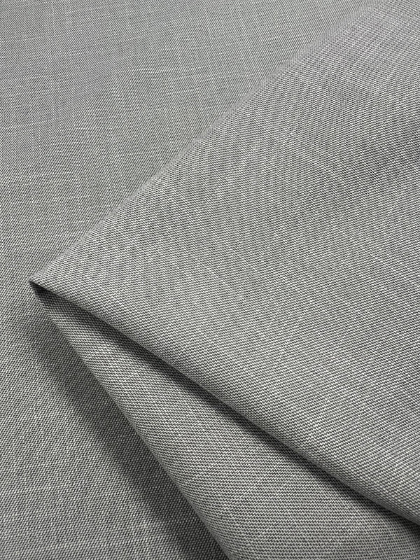A close-up image of a light gray, slightly textured fabric. The Textured Cotton Suiting - Grey - 150cm by Super Cheap Fabrics is folded neatly, showcasing its smooth surface and fine weave. Ideal for formal suits, the versatile fabric's lighting highlights faint patterns and gives a sense of its soft and elegant texture.