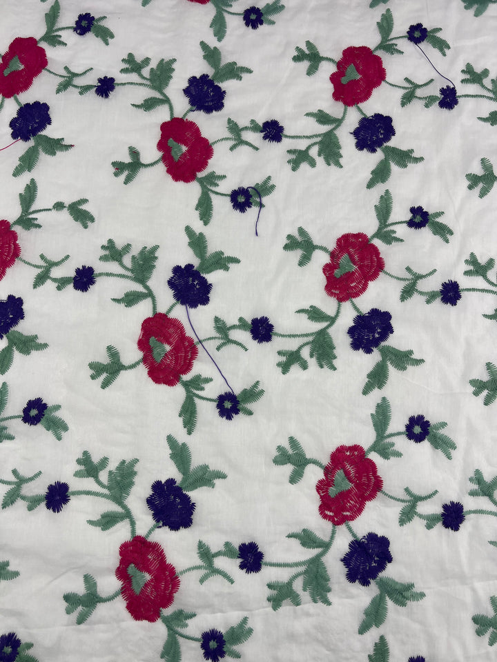 A lightweight cotton fabric with an embroidered floral pattern featuring red and dark blue flowers with green leaves on a white background, the Embroidered Cotton - Pinkle Vines - 145cm by Super Cheap Fabrics.