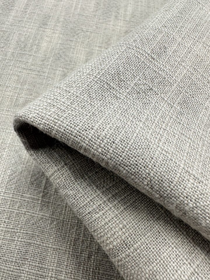 Close-up of a folded piece of Basket Dyed Cotton in Dove, highlighting its textured twill weave pattern. The fabric, by Super Cheap Fabrics, reveals a detailed structure and subtle tone variations typical of upholstery fabric.