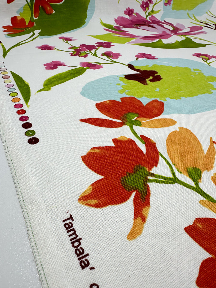 A detailed image showcasing a sample of the "Blended Duck - Tambala - 150cm" fabric from Super Cheap Fabrics, featuring bold red, orange, pink, and green flowers on a linen cotton blend against a white backdrop. Along the edge, there's a strip with colored dots that serves as a color guide for this medium weight duck fabric, ideal for home décor accessories.