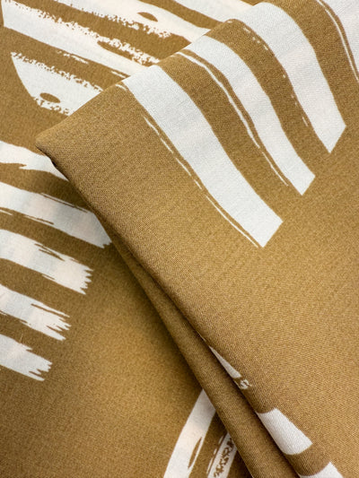 A close-up of folded Designer Rayon - Modern Earth (145cm) by Super Cheap Fabrics, featuring an abstract white brushstroke pattern on brown for a modern, artistic look—ideal for vibrant, contemporary projects.