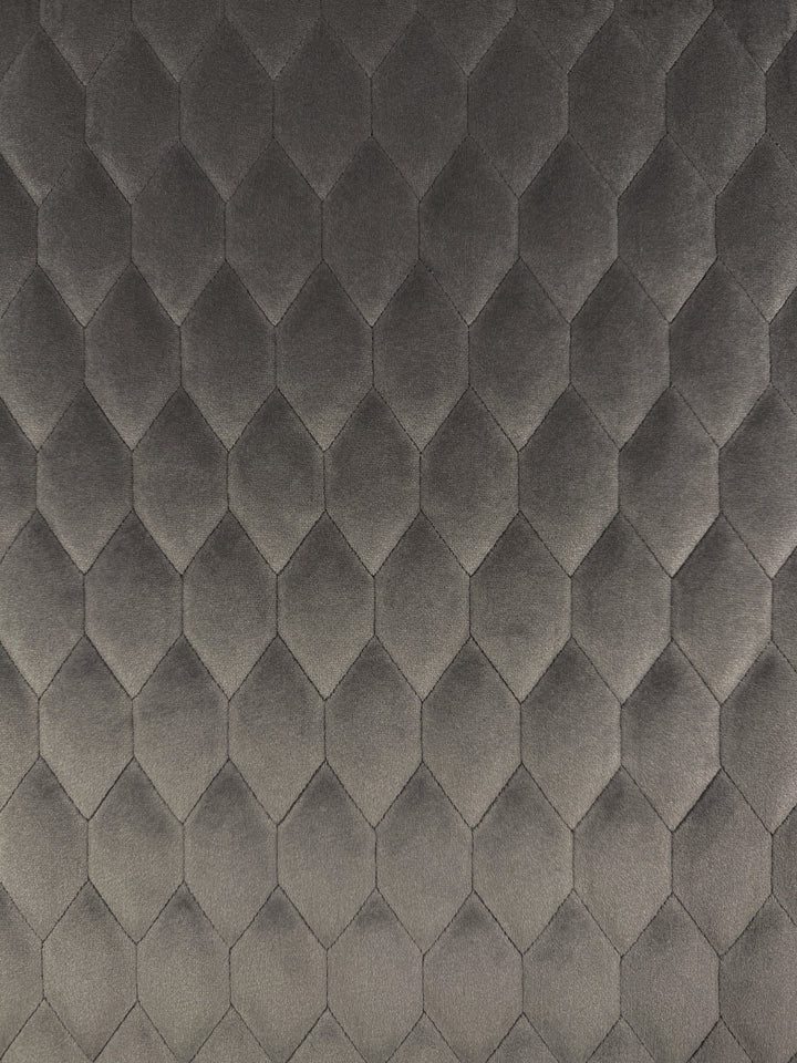 Super Cheap Fabrics’ Quilted Velvet - Vintage Khaki (145cm) features a gray, three-dimensional textured velvet with a repeating hexagonal quilted pattern, ideal for upholstery and enhanced by lighting that highlights the geometric design.