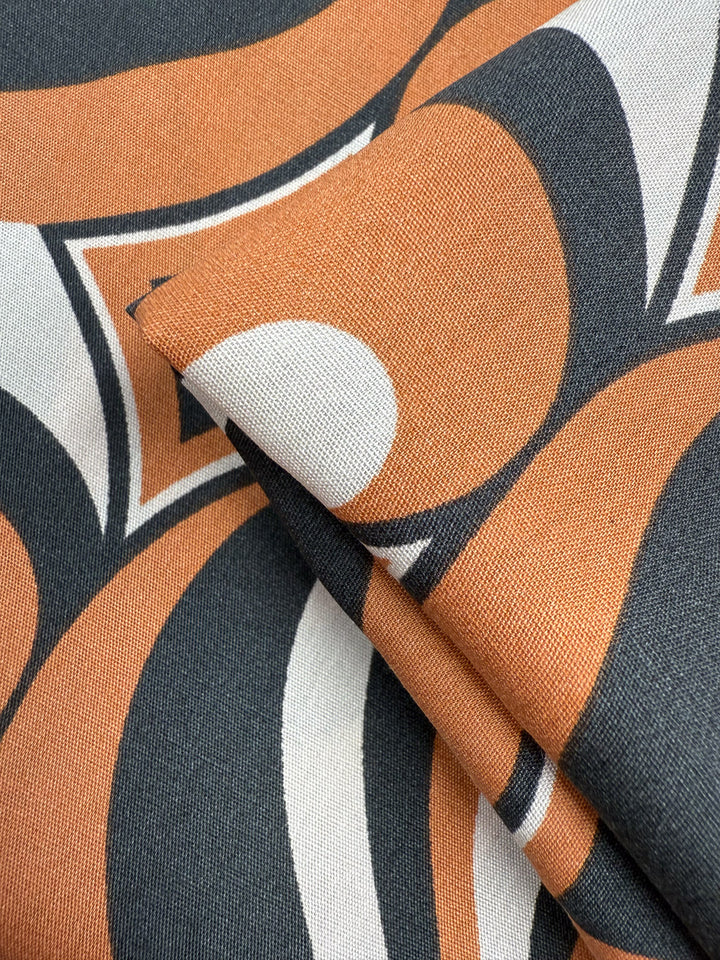 Close-up of Designer Rayon - Retro Swirl (142cm) by Super Cheap Fabrics, showcasing a bold retro pattern in orange, black, and white with overlapping curved and circular shapes for a vibrant look.