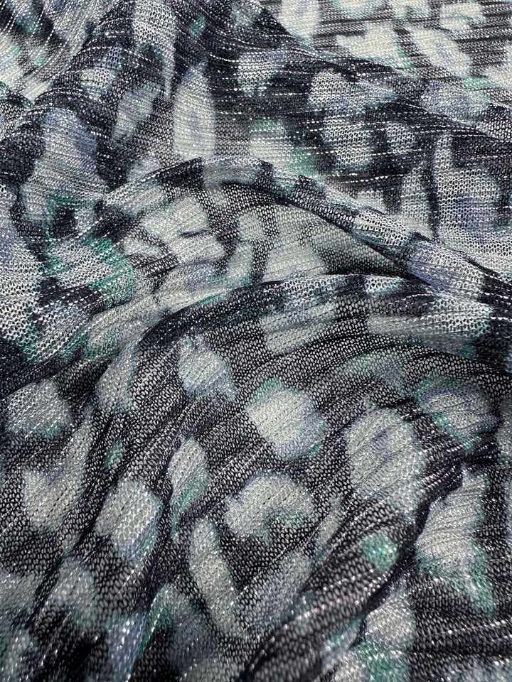 Close-up of the Metallix Pleat fabric in Ocean Leopard by Super Cheap Fabrics, featuring an abstract pattern with brush strokes or a floral motif in shades of gray, black, and white. Made from lightweight polyester, this 140cm wide material appears soft and slightly reflective with hints of navy woven throughout.