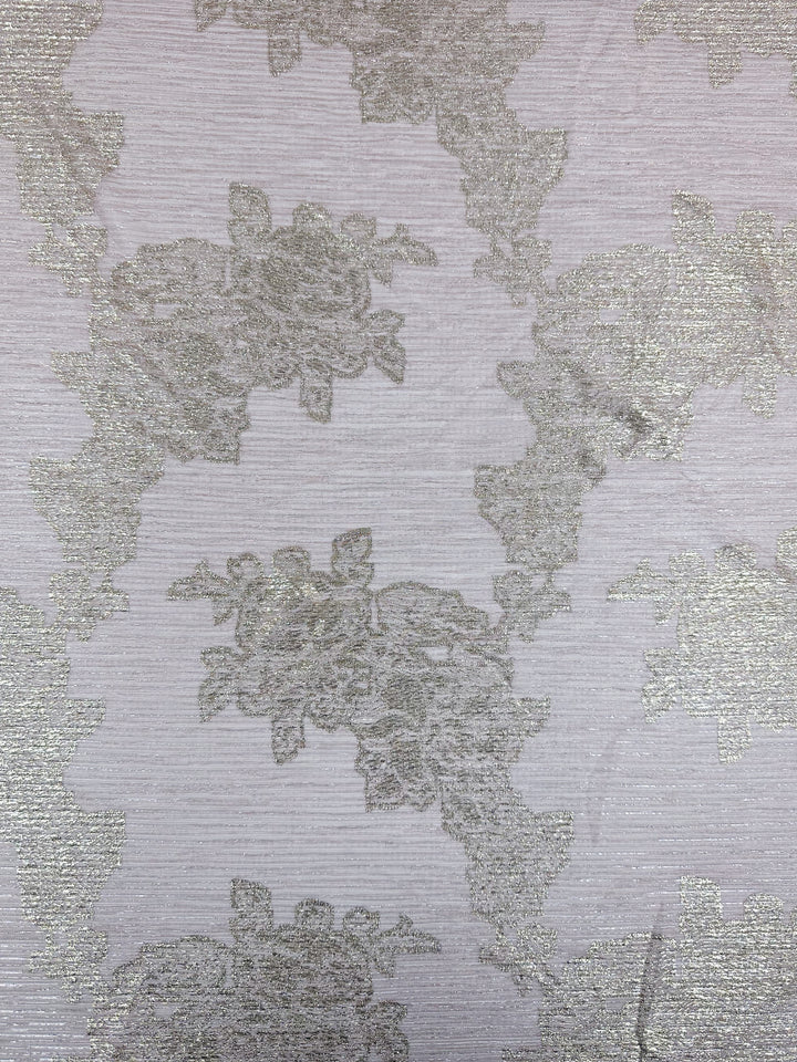 Close-up of the Metallix Pleat - Gold Leaf fabric by Super Cheap Fabrics. This light beige polyester textile features intricate floral embroidery. The elegant pattern of flowers and leaves is subtly highlighted with hints of baby pink, adding sophistication to its lightweight appearance.