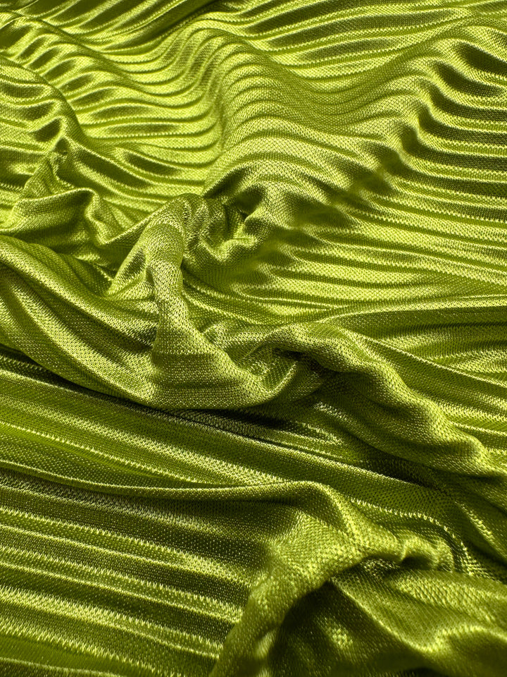 A close-up of the Metallix Pleat - Chartreuse - 140cm fabric from Super Cheap Fabrics showcases a textured, ribbed pattern. This lightweight polyester material appears smooth and glossy, with draped folds creating dynamic shadows and highlights.