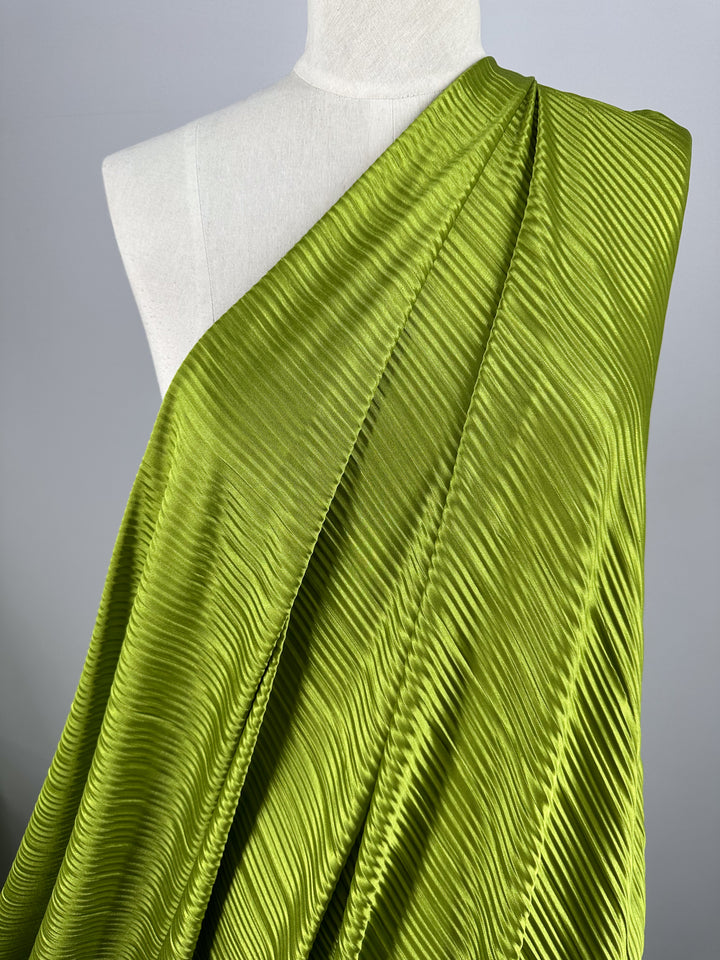 A close-up of a mannequin draped with Super Cheap Fabrics' Metallix Pleat in Chartreuse, measuring 140cm, which showcases a vibrant pleated polyester fabric with a shiny texture. Styled diagonally across the form, this lightweight fabric beautifully highlights its rich color and intricate details.