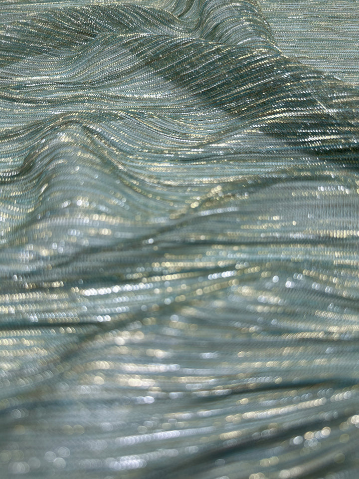 Close-up of the Metallix Pleat - Mermaid Glitter fabric by Super Cheap Fabrics, featuring a shimmering light blue polyester with metallic gold threads that form a textured, wavy pattern. This lightweight material reflects light for a shiny and glossy effect.