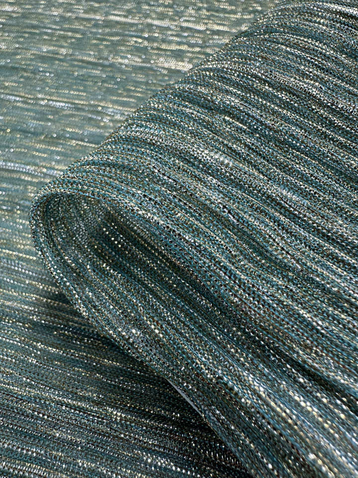 A close-up of the Metallix Pleat - Mermaid Glitter - 140cm from Super Cheap Fabrics shows a lightweight polyester fabric with a metallic sheen in shades of silver and blue, featuring tightly woven horizontal lines and a softly undulating surface.