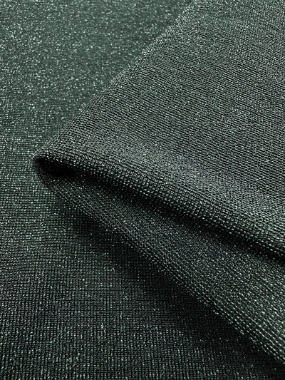 The close-up of the Folded Metallic Lycra from Super Cheap Fabrics, with its dark green hue and subtle sparkle reminiscent of a luxurious green jacket, reveals a fine weave and soft sheen. This fabric's smooth and elegant appearance makes it ideal for crafting chic dresses. With a width of 170cm, it's perfect for your next creation.