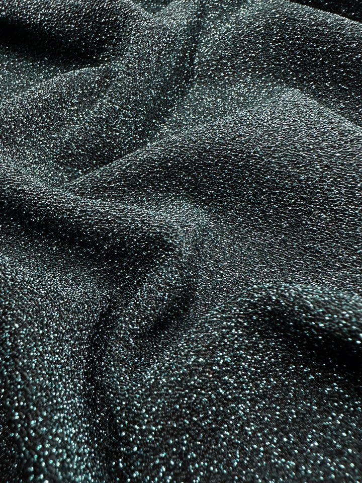 The Metallic Lycra - Aqua Fuzz from Super Cheap Fabrics showcases a close-up of its shimmering surface, featuring textured sparkle that captures the light like rippling waves on an aqua sea. This 170cm wide fabric displays subtle undulating folds, perfect for creating dazzling dresses.