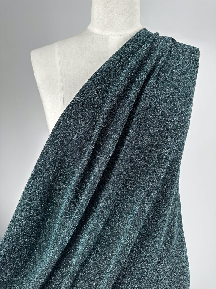 A mannequin displays fabric from Super Cheap Fabrics, featuring Metallic Lycra in Aqua Fuzz, measuring 170cm, elegantly arranged asymmetrically over one shoulder against a plain gray background.