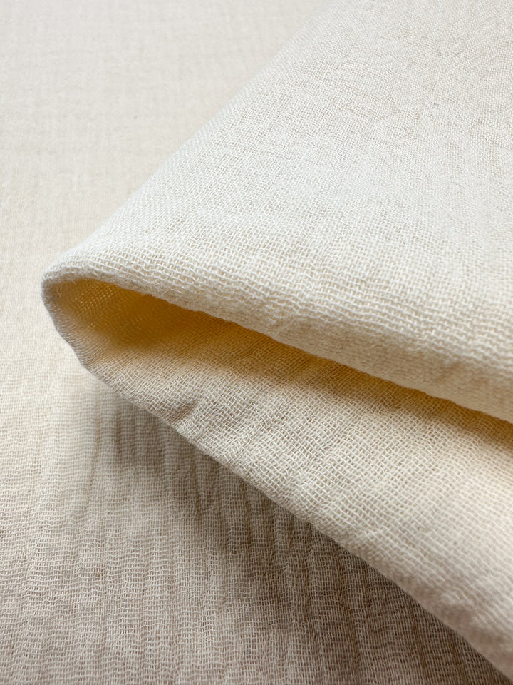 Close-up of a folded piece of Muslin - Almond Milk - 135cm by Super Cheap Fabrics. This organic material showcases a soft texture with a visible weave pattern, making it ideal for reusable applications.